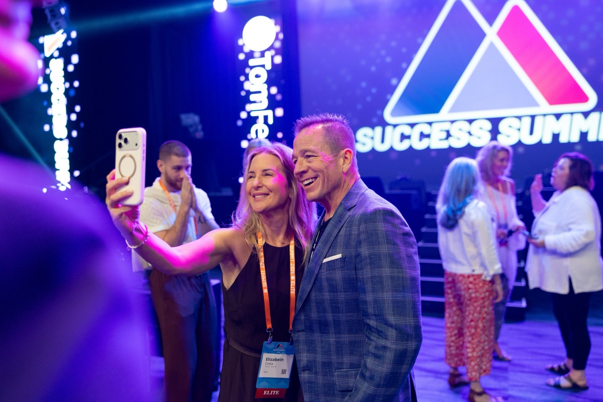 A member grabbing a selfie with Aaron under the Success Summit screen